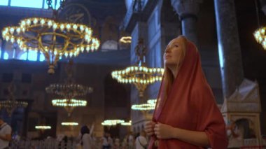 Kafası atkıya sarılı bir kadın turist, tapınakların görkemli ihtişamına dalmış, Ayasofya İstanbullarının kutsanmış güzelliği içinde huşu içinde duruyor. Yavaş çekim videosu