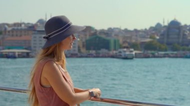 Şapka takan genç bir kadın turist, İstanbul 'un kalbi İstanbul Boğazı' nda dolaşırken Asya ve Avrupa 'nın kıyıları boyunca birleşmesine hayret ediyor.