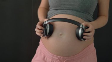 A serene expectant mother attaches wireless headphones to her belly and plays soothing music for her unborn baby, sharing a moment of bonding.