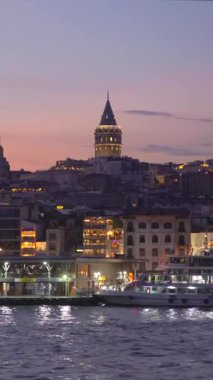 Alacakaranlıkta tekneyle sakin bir yolculuk İstanbullar 'ın ikonik Galata Kulesi' nin çarpıcı bir görüntüsünü sunuyor. Şehrin ufuk çizgisi üzerinde görkemli bir şekilde yükseliyor.