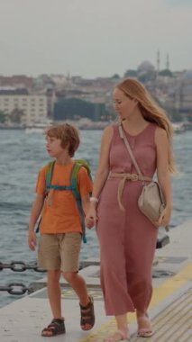 Galataport 'un canlı atmosferine dalan genç bir kadın ve oğlu turistler, iskele boyunca neşeli bir yürüyüşle İstanbul' un cazibesine kapılıyor. Yavaş çekim videosu. Dikey biçim
