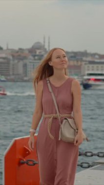 Galataport 'un canlı atmosferine dalan genç bir kadın turist, iskele boyunca neşeli bir yürüyüşle İstanbul' un cazibesine kapılıyor. Dikey video