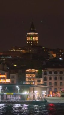 Gece çöktüğünde İstanbul 'da feribot yolculuğuna çıkın. Şehir merkezinin çarpıcı manzarası ve aydınlık Galata Kulesi ufuk çizgisini süslüyor. Dikey video