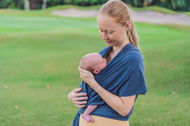 Annem yeni doğmuş bebeğiyle askıda yürüyor. Bu an, anne ve çocuk arasındaki yakın bağın altını çiziyor. Günlük hayatta rahatlığı, güvenliği ve bebek giyiminin faydalarını destekliyor..