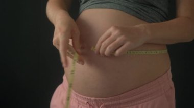 Hamile bir kadının göbeğini mezurayla ölçerken çekilmiş yakın plan bir fotoğrafı. Video nazik ve dikkatli hareketleri yakalıyor. Hamileliğin heyecanını ve beklentisini vurguluyor.