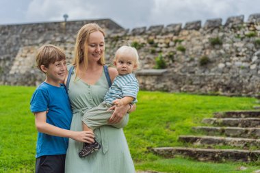 Mother with her toddler and teenage sons exploring Fuerte de San Felipe de Bacalar. Family travel, cultural heritage, and historical adventure concept. clipart