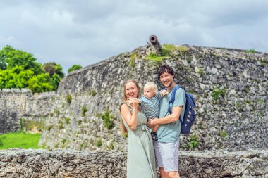 Mom, dad and their baby son exploring Fuerte de San Felipe de Bacalar. Family travel, cultural heritage, and historical adventure concept. clipart