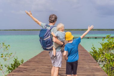 Baba ve küçük çocukları Meksika 'daki Bacalar Gölü' nün turkuaz sularında ahşap iskeleyi keşfediyorlar. Huzurlu tropikal seyahat konsepti.