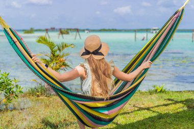 Bacalar Gölü 'nün turkuaz sularının arka planında hamakta oturan dişi turist. Aile bağı, yaz tatili ve Quintana Roo 'da açık hava eğlencesi, Meksika konsepti..