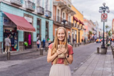 Meksika, Puebla 'da bir koloni caddesinde churro yiyen kadın turist. Kültürel deneyim, yerel mutfak ve sokak yemekleri keşfi konsepti.