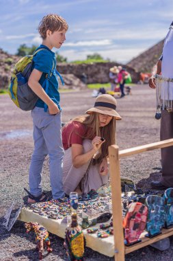 Anne ve oğul turistler Teotihuacan piramidinin dibindeki bir sokak satıcısından Meksikalı hediyelik eşya alıyorlar. Kültürel deneyim, seyahat ve yerel zanaat konsepti.