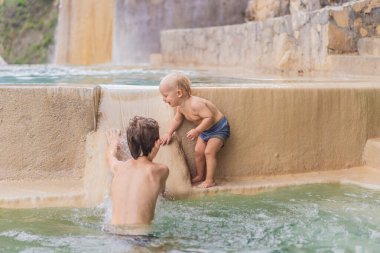 Toddler and teenage boys bathing in the hot springs of Grutas Tolantongo, Mexico. Family adventure, relaxation, and natural wellness concept. clipart