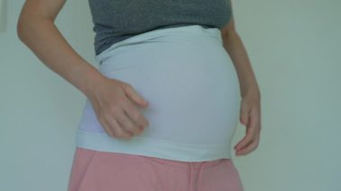 Müstakbel anne, bebeğini yumuşak bir bandajla kucaklıyor ve nazik bir destek sağlıyor. Doğum rahat ettirdi. Yavaş çekim videosu.