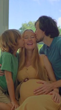 Genç ve hamile bir kadının, kocasıyla büyük oğlu arasında bir koltuğa kurulmuş, aile anının tadını çıkarırken, hepsi sohbete dalmış ve anneyi öperken görüntüler.