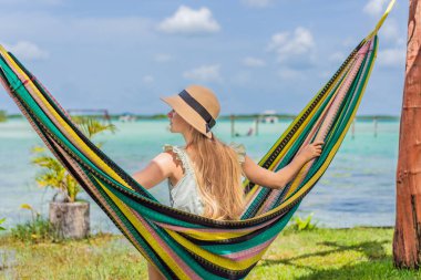 Bacalar Gölü 'nün turkuaz sularının arka planında hamakta oturan dişi turist. Aile bağı, yaz tatili ve Quintana Roo 'da açık hava eğlencesi, Meksika konsepti..