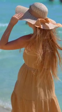 Güzel, hamile bir kadın berrak mavi suyla çarpıcı bir kumsalda yürüyor. Yumuşak dalgaların ve ayaklarının altındaki sıcak kumların tadını çıkarıyor. Bebeğini beklemenin verdiği neşe ve beklentiyi yansıtıyor.