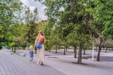 Anne ve küçük oğlu parkta yürüyorlar. Aile bağları, açık hava keşifleri ve ebeveynlik kavramı..