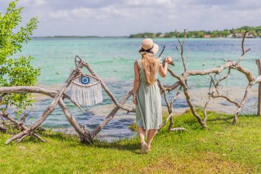 Female tourist in a turquoise dress standing on a wooden pier over the turquoise waters of Bacalar Lake, Mexico. Peaceful tropical travel destination concept. clipart