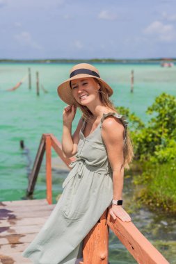 Female tourist in a turquoise dress standing on a wooden pier over the turquoise waters of Bacalar Lake, Mexico. Peaceful tropical travel destination concept. clipart