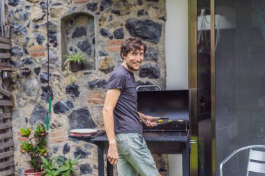 Adam arka bahçesindeki barbeküde yemek pişiriyor. Açık hava yemekleri, ev hayatı ve aile zamanı konsepti..