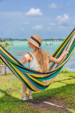 Bacalar Gölü 'nün turkuaz sularının arka planında hamakta oturan dişi turist. Aile bağı, yaz tatili ve Quintana Roo 'da açık hava eğlencesi, Meksika konsepti..