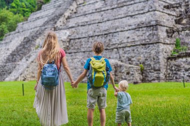 Mother with her toddler and teenage sons exploring the ancient pyramids of Palenque, Mexico, surrounded by dense jungle. Cultural heritage and adventure travel concept. clipart