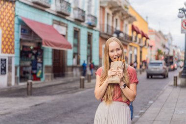 Meksika, Puebla 'da bir koloni caddesinde churro yiyen kadın turist. Kültürel deneyim, yerel mutfak ve sokak yemekleri keşfi konsepti.