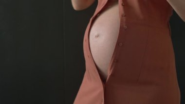 Hamile bir kadın, gelişmekte olan karnını elbisesine sığdırmak için çabalıyor ve hamileliği boyunca vücut değişikliklerinin zorluklarını vurguluyor. Bu uygun ve esprili an rahat olma ihtiyacını yansıtıyor.