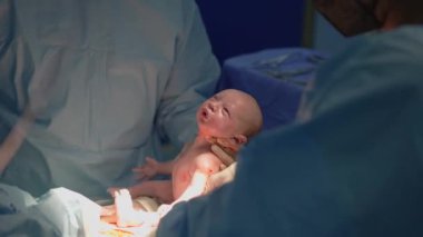 Yeni doğmuş bir bebek sezaryen sırasında annesinin karnından dikkatlice kaldırılır. Yaşamın başlangıcını, tıbbi hassasiyeti ve doğum mucizesini yakalayan güçlü bir an.