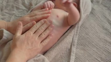 Banyodan sonra anne yeni doğan bebeğine nazikçe masaj yapar ve bebekler için cilt yağı sürer. Bebek konforu, rahatlama ve sağlıklı cilt için hassas bir bağ ve bakım anı.