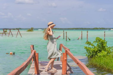 Female tourist in a turquoise dress standing on a wooden pier over the turquoise waters of Bacalar Lake, Mexico. Peaceful tropical travel destination concept. clipart