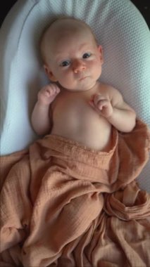Yeni doğmuş bir bebek, yumuşak çarşafla örtülü, rahat bir bebek kozasında huzur içinde yatar. Huzurlu ve rahat bir an. Bebeklerin ilk günleri için rahatlık ve ilgiyi ön plana çıkarıyor.