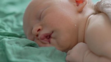 Uyuyan yeni doğmuş bir bebeğin yumuşak bir muslin battaniyeye sarılı olduğu yakın çekim videosu. Yumuşak ve huzurlu bir an, yeni doğmuş bir bebeğin masumiyetini ve huzurunu yakalıyor.