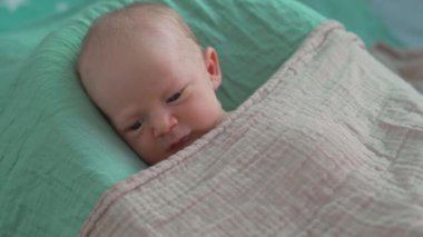 Yeni doğmuş bir bebek, yumuşak çarşafla örtülü, rahat bir bebek kozasında huzur içinde yatar. Huzurlu ve rahat bir an. Bebeklerin ilk günleri için rahatlık ve ilgiyi ön plana çıkarıyor.