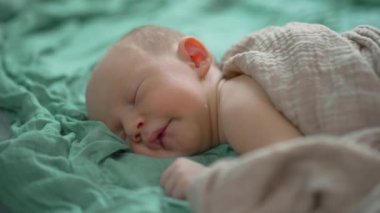 Uyuyan yeni doğmuş bir bebeğin yumuşak bir muslin battaniyeye sarılı olduğu yakın çekim videosu. Yumuşak ve huzurlu bir an, yeni doğmuş bir bebeğin masumiyetini ve huzurunu yakalıyor.