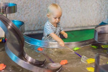 Küçük çocuk bir eğlence merkezinde canlı bir su oyun alanında oyuncak balık yakalıyor. Genç çocuklara ilham vermek için tasarlanmış eğlenceli bir öğrenme, oyun ve keşif anı..