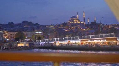 22.08.2022 - ISTANBUL, TURKEY: Gece aydınlatılmış Galata Köprüsü 'nün feribotundan çarpıcı bir görüntü, canlı şehir ışıkları ve su üzerindeki yansımaları gösteriyor.