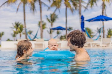Bir baba havuzda oğlu ve bebeğiyle birlikte yüzmekten zevk alır. Çocuk güvenli bir şekilde şişme bir bebek arabasının içine yerleştirilir. Eğlenceli aile bağları, yaz rahatlığı ve ebeveynlik kavramı.