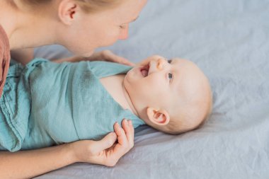 Bir anne bebeğini nazikçe yumuşak bir muslin kundağına sarıp sıcak ve rahat hissettirir. Anne ve çocuk arasında şefkatli bir ilgi ve sevgi anı. Annelik, bebek bakımı ve yetiştirme konsepti.