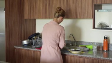Genç bir kadın mutfakta bulaşıkları yıkıyor, temizlik ve düzene odaklanıyor. Basit ve uyumlu bir ev yapımı, ev bakımı ve düzenli bir ev ortamı.