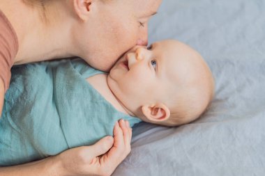 Bir anne bebeğini nazikçe yumuşak bir muslin kundağına sarıp sıcak ve rahat hissettirir. Anne ve çocuk arasında şefkatli bir ilgi ve sevgi anı. Annelik, bebek bakımı ve yetiştirme konsepti.
