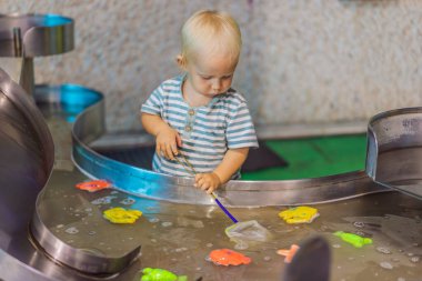Küçük çocuk bir eğlence merkezinde canlı bir su oyun alanında oyuncak balık yakalıyor. Genç çocuklara ilham vermek için tasarlanmış eğlenceli bir öğrenme, oyun ve keşif anı..