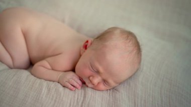 Uyuyan yeni doğmuş bir bebeğin yumuşak bir muslin battaniyeye sarılı olduğu yakın çekim videosu. Yumuşak ve huzurlu bir an, yeni doğmuş bir bebeğin masumiyetini ve huzurunu yakalıyor.