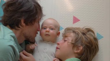 Bir baba ve ağabey yeni doğmuş bebeklerini yerde bebek yatağında nazikçe öperler. Güzel bir aile sevgisi, şefkat ve huzur dolu bir bağ anı.