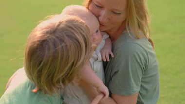 Genç bir anne, yemyeşil bir çimenlikte büyük oğlu ve yeni doğmuş çocuğuyla güneşli bir günün tadını çıkarır. Sevgi, bağ ve açık hava eğlencesiyle dolu neşeli bir aile anı ebeveynliği ve çocukluğu kutluyor.