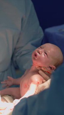 Yeni doğmuş bir bebek sezaryen sırasında annesinin karnından dikkatlice kaldırılır. Yaşamın başlangıcını, tıbbi hassasiyeti ve doğum mucizesini yakalayan güçlü bir an.
