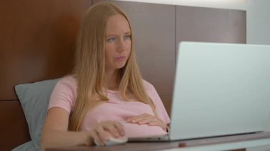 8.-9. ayındaki hamile kadın laptopuyla yataktan çalışıyor, iş ve hamileliği dengeliyor. Uzaktan çalışma, verimlilik ve doğum öncesi bakımı yönetmek