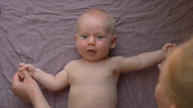 Bir anne yeni doğmuş bebeğiyle nazikçe jimnastik yapar, bebek kollarını ve bacaklarını hafifçe hareket ettirir. Bağ kurmayı, esnekliği ve bebek refahını teşvik eden hassas ve besleyici bir faaliyet.