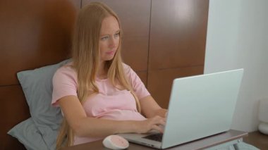 8.-9. ayındaki hamile kadın laptopuyla yataktan çalışıyor, iş ve hamileliği dengeliyor. Uzaktan çalışma, verimlilik ve doğum öncesi bakımı yönetmek
