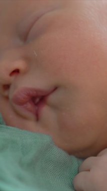 Uyuyan yeni doğmuş bir bebeğin yumuşak bir muslin battaniyeye sarılı olduğu yakın çekim videosu. Yumuşak ve huzurlu bir an, yeni doğmuş bir bebeğin masumiyetini ve huzurunu yakalıyor.